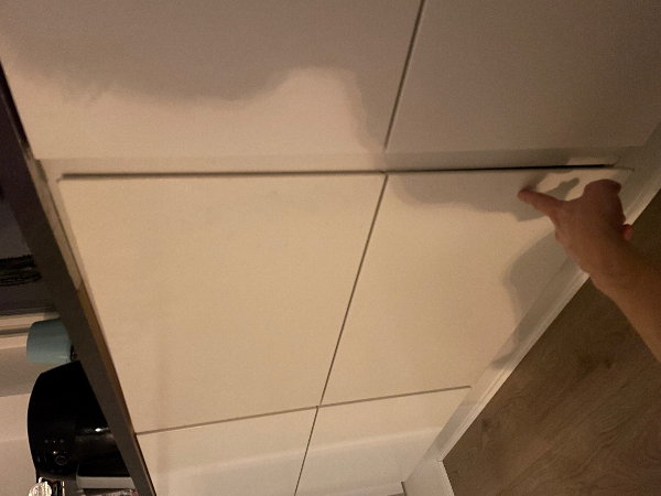 En køkkenlåge der hænger, og som delvist er faldet af pga. hængsler der er rykket ud af skabet