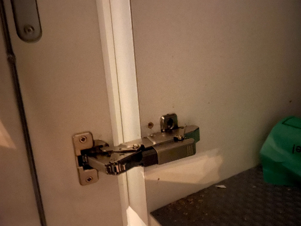 En køkkenlåge der hænger, og som delvist er faldet af pga. hængsler der er rykket ud af skabet