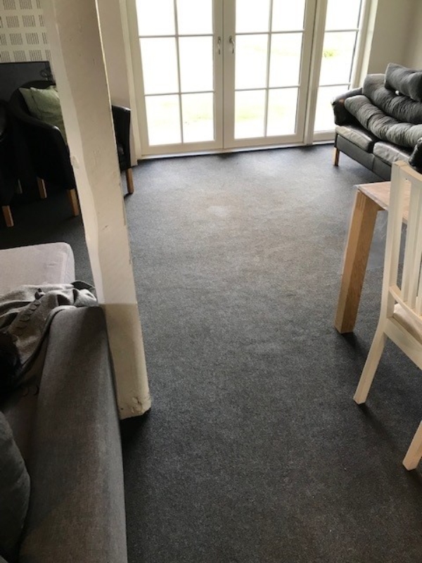 Fuldlimet gulvtæppe i fliser 50 x 50 cm. 36 m2 med stolpe ca. midt i rummet og én havedør.